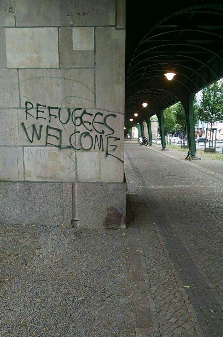 stone building wall next to a covered archway, the wall has 'REFUGEES WELCOME' graffitied on it